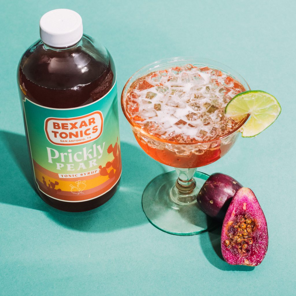 bottle of prickly pear tonic syrup with cocktail and fresh prickly pears
