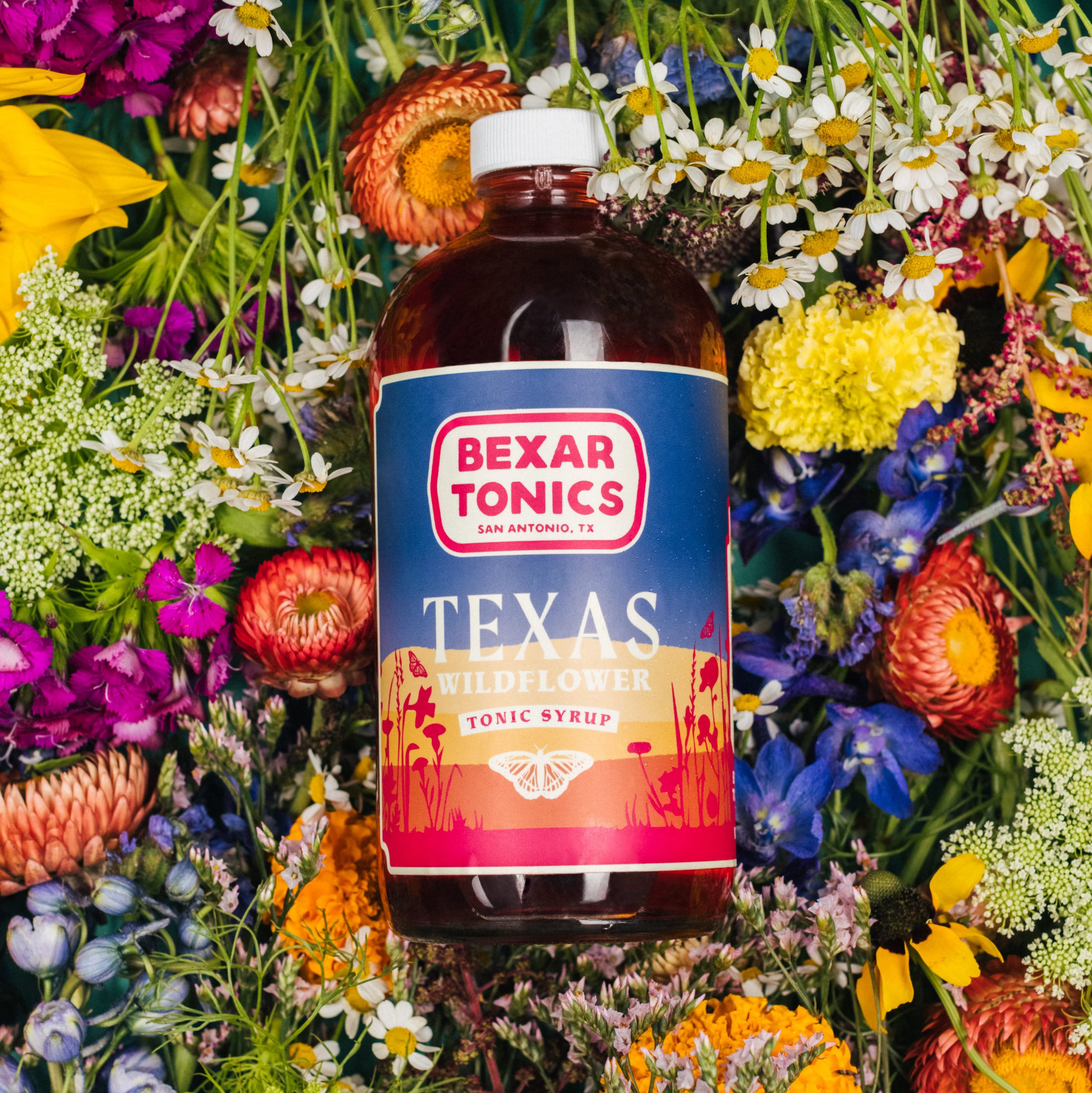 bottle of wildflower tonic syrup surrounded by wildflowers